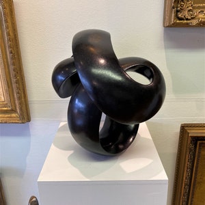 May include: A black, abstract sculpture made of smooth, curved forms. The sculpture is displayed on a white pedestal.
