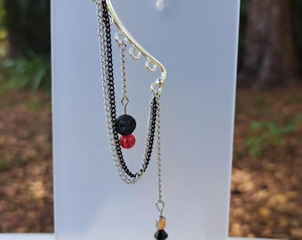 May include: Silver ear cuff with three chains, a black lava rock bead, a red bead, and a black and clear crystal dangle.