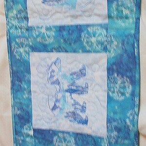 Op de afbeelding: Een blauwe en witte quilted wanddecoratie met drie geborduurde afbeeldingen van gestileerde olifanten. De stof heeft een tie-dye patroon.