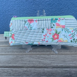 May include: A small, quilted zippered pouch with a patchwork design featuring floral and striped patterns in shades of blue, green, and pink.