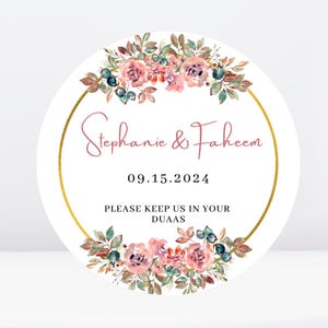Pode incluir: Um adesivo redondo branco para lembrancinhas de casamento com uma borda circular dourada e um design de coroa de flores. O texto "Stephanie & Faheem" está escrito em fonte rosa cursiva. A data "09.15.2024" está escrita abaixo dos nomes. O texto "Por favor, mantenha-nos em suas Duas" está escrito abaixo da data.