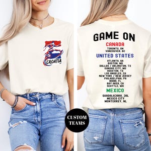 A woman wearing a white t-shirt with a graphic of a red, white, and blue figure on it, along with text that lists the locations of various events related to Croatia.