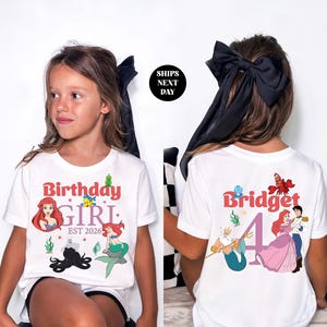 A young girl wearing a white t-shirt with a personalized design and text, including a mermaid character and the number 4.