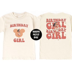 Pu&ograve; includere: T-shirt color crema con un design retr&ograve;. La parte anteriore presenta le parole "BIRTHDAY GIRL" in rosso, con un personaggio dei cartoni animati al centro. Il retro della maglietta ripete le parole "BIRTHDAY GIRL" in uno stile simile. &Egrave; visibile anche un cerchio nero con testo bianco.
