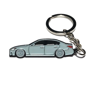 May include: A silver metal keychain featuring a light gray car with black wheels and red taillights. The car is in a side profile view.