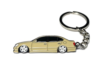 May include: A beige car keyring with a silver key ring and chain. The car is a saloon with black windows and wheels.