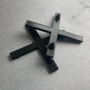 May include: Two black plastic crosses with rounded edges and small raised bumps on the ends of each arm.
