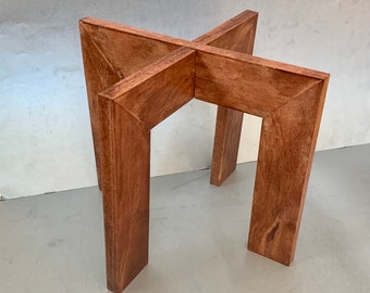 Puede incluir: Una base de mesa de madera con un diseño en forma de cruz. La base está hecha de cuatro piezas de madera que se unen en el centro. La madera es de color marrón oscuro y tiene un acabado liso.