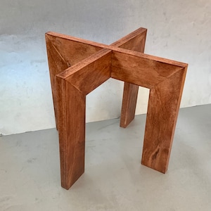 May include: A wooden table base with a cross-shaped design. The base is made of four pieces of wood that are joined together at the center. The wood is a rich brown color and has a smooth finish.