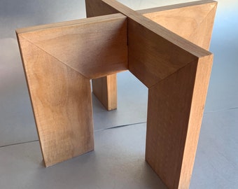 Puede incluir: Una base de mesa de madera con un diseño en forma de cruz. La base está hecha de madera marrón claro y tiene un estilo simple y moderno.