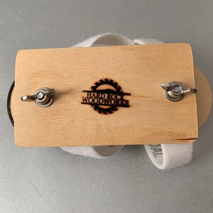 May include: A wooden sanding block with two metal knobs and a white sanding pad. The block has the text "Hard Rock Woodworks" burned into the wood.