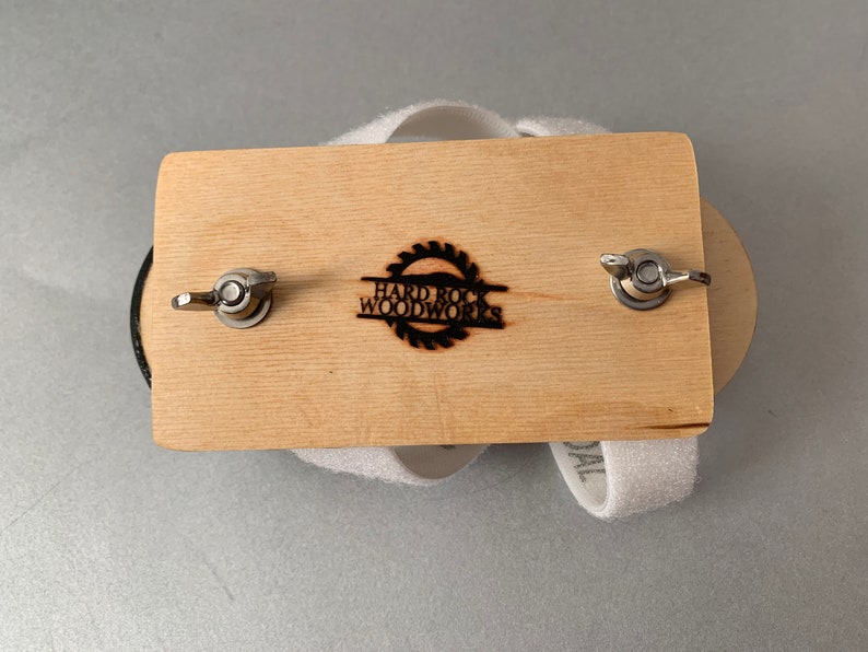 May include: A wooden sanding block with two metal knobs and a white sanding pad. The block has the text "Hard Rock Woodworks" burned into the wood.