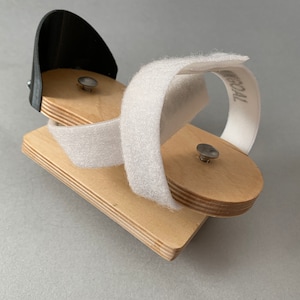 May include: A wooden foot support with a black plastic piece and white velcro straps. The straps are labeled "MEDICAL".