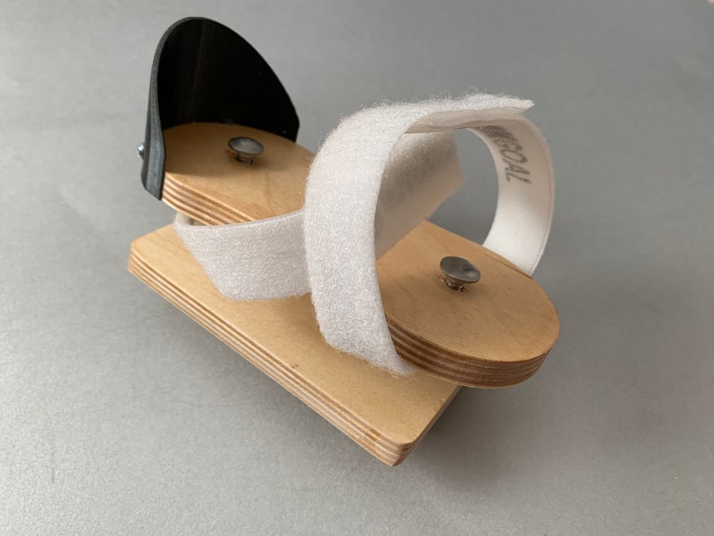 May include: A wooden foot support with a black plastic piece and white velcro straps. The straps are labeled "MEDICAL".