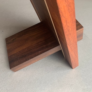Puede incluir: Un marco de fotos de madera con un acabado marr&oacute;n oscuro y una incrustaci&oacute;n de madera clara. El marco tiene un soporte en la parte posterior para sostenerlo.