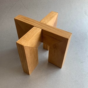 May include: A wooden stand with a cross-shaped design. The stand is made of light brown wood and has a smooth finish.