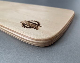May include: A close-up of the edge of a light wood cutting board with rounded edges. The board is made of plywood and has a laser-etched logo that reads "Jess & Co. Woodworks".