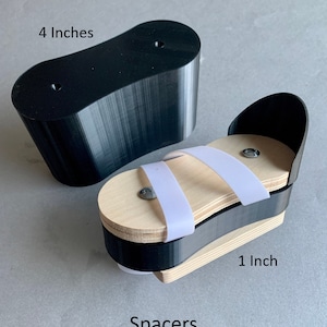 May include: Two black 3D printed spacers, one 4 inches long and the other 1 inch long. The smaller spacer has a wooden platform with white elastic straps. The spacers are labeled "Spacers".