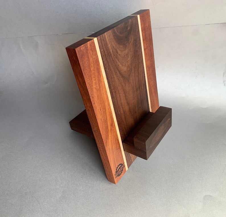 Puede incluir: Un soporte de tel&eacute;fono de madera con acabado en nogal y caoba. El soporte tiene un peque&ntilde;o estante para sostener un tel&eacute;fono y una base m&aacute;s grande para la estabilidad. El soporte est&aacute; hecho de madera maciza y tiene un acabado natural.