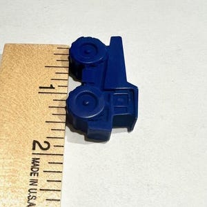 May include: A blue plastic toy truck measuring approximately 1 inch in length. The truck has a flatbed and four wheels.