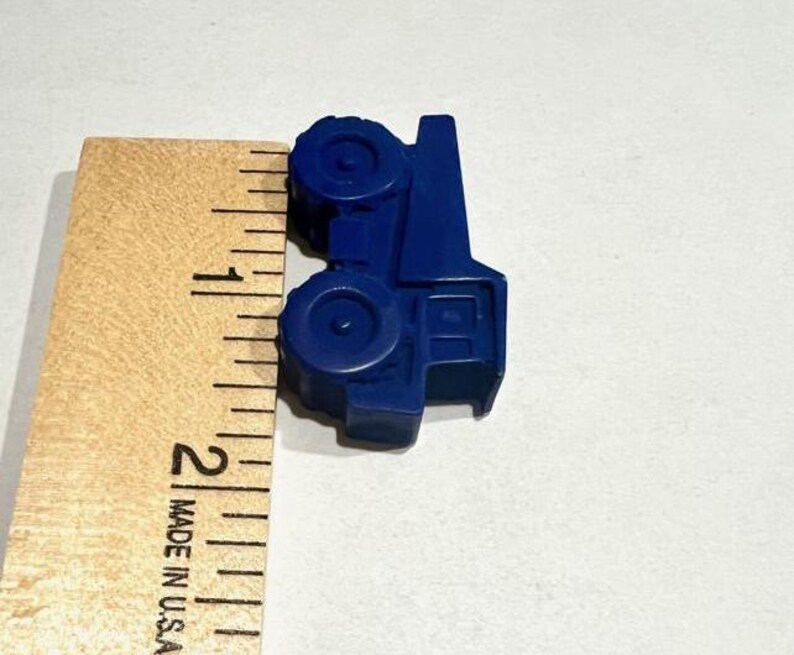 May include: A blue plastic toy truck measuring approximately 1 inch in length. The truck has a flatbed and four wheels.