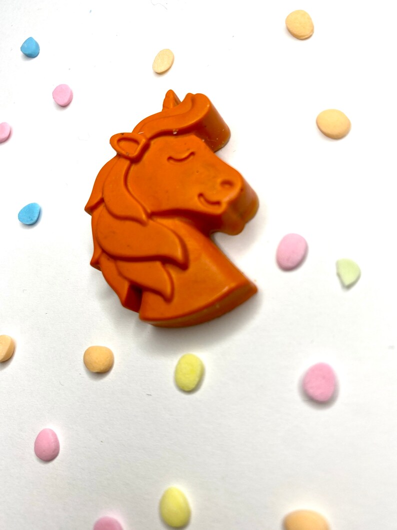 May include: Orange unicorn shaped candle with a white background and colorful confetti.