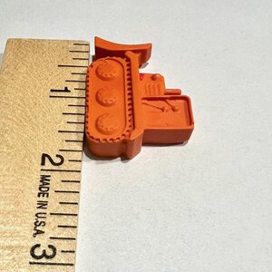 May include: Orange plastic toy bulldozer measuring approximately 2 inches in length. The bulldozer has a detailed design with tracks and a raised blade.