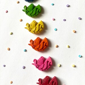 May include: Six unicorn-shaped crayons in a rainbow of colors: blue, green, yellow, orange, pink, and red. The crayons are arranged vertically on a white background with colorful confetti.