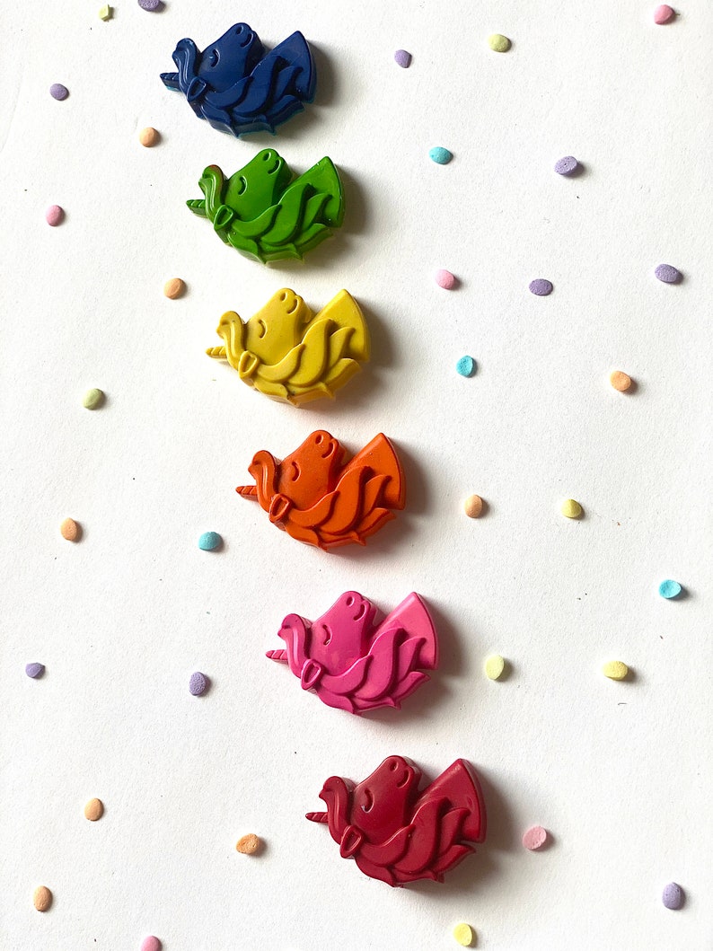 May include: Six unicorn-shaped crayons in a rainbow of colors: blue, green, yellow, orange, pink, and red. The crayons are arranged vertically on a white background with colorful confetti.