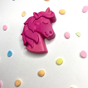 May include: A pink unicorn shaped crayon surrounded by colorful confetti.