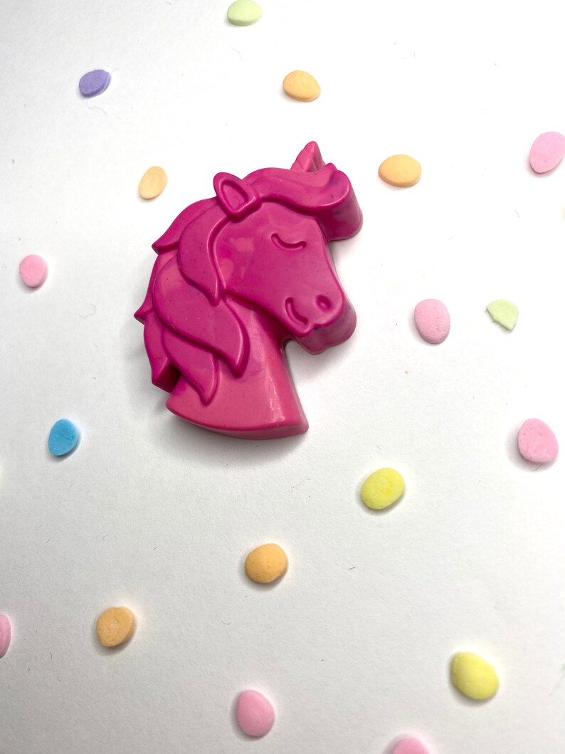 May include: A pink unicorn shaped crayon surrounded by colorful confetti.