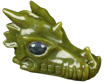 Puede incluir: Una escultura de cabeza de dragón de jade verde con un ojo azul. La boca del dragón está abierta y sus dientes son visibles. La escultura está pulida y tiene un acabado brillante.