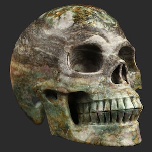 May include: A green, brown and white carved stone skull with detailed features, including teeth. The skull is made from a type of stone with a swirling pattern.