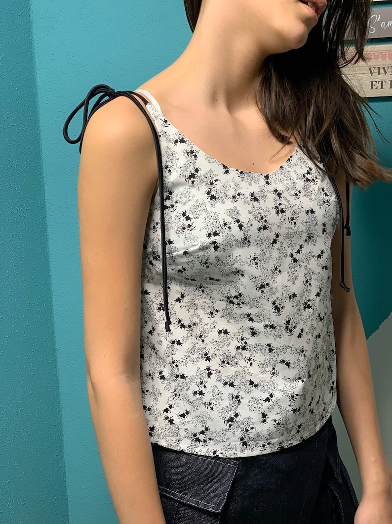 May include: A white tank top with a black floral print and adjustable straps. The straps are tied at the shoulders.