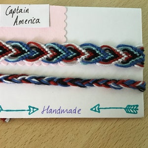 May include: Two handmade bracelets in red, white and blue colours. The top bracelet is a woven design and the bottom bracelet is a braided design. The card says "Captain America" and "Handmade".