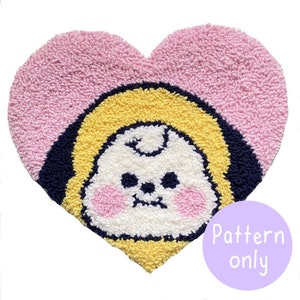 May include: A pink heart-shaped rug with a yellow and white cartoon character in the center. The character has a white face with black eyes and a pink nose. The rug has a navy blue border.
