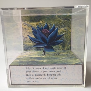 May include: A black lotus flower in a clear acrylic cube. The flower is surrounded by a green and yellow background. The text on the base reads: "Adds 3 mana of any single color of your choice to your mana pool, then is discarded. Tapping this artifact can be played as an interrupt."