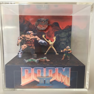 May include: A 3D diorama of the video game Doom II. The diorama features a red background with a demon, a player character, and a fallen soldier. The diorama is in a clear acrylic cube with the words "DOOM II" printed on the base.