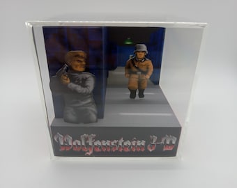 May include: A clear plastic display case with a diorama inside. The diorama depicts a scene from the video game Wolfenstein 3-D. The scene features two figures, one in a grey uniform and the other in a brown uniform. The text "Wolfenstein 3-D" is printed on the base of the diorama.