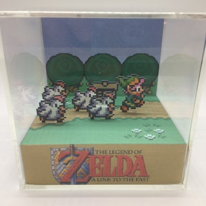 May include: A clear acrylic box diorama featuring a pixelated Link from The Legend of Zelda: A Link to the Past video game. Link is running through a forest with a group of chickens. The box has a brown base with the game's logo and title.