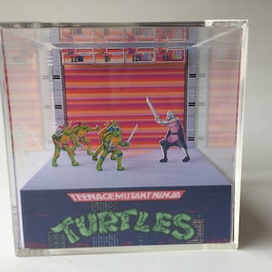 May include: A diorama of the Teenage Mutant Ninja Turtles video game. The diorama features four green turtles with swords, fighting a purple-clad villain with a sword. The diorama is set against a pixelated background with the words "Teenage Mutant Ninja Turtles" and "TURTLES" printed on the base.