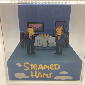 May include: A 3D diorama of a scene from the Simpsons TV show. The diorama features two characters, Mr. Burns and Waylon Smithers, standing in a room with a table and chairs. The text "STEAMED HAMS" is written on the base of the diorama.