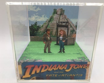 May include: A 3D diorama of a scene from the video game Indiana Jones and the Fate of Atlantis. The diorama features Indiana Jones and a female character standing in front of a Mayan pyramid with a sign that reads "Trinkets".