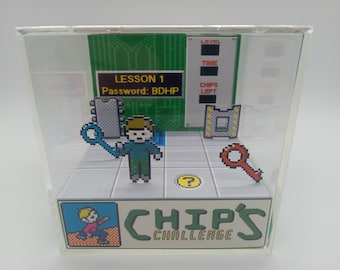 May include: A miniature diorama of a video game called "Chip's Challenge". The diorama features a pixelated character holding a blue key, a green screen with the text "LESSON 1 Password: BDHP", and a red key on the floor. The diorama is enclosed in a clear acrylic box.