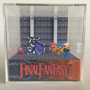May include: A clear acrylic display cube featuring a pixelated scene from Final Fantasy. The scene includes characters and the game's logo. The background depicts a castle interior with columns and a stone floor.