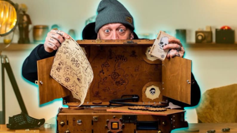 Puede incluir: Un cofre del tesoro de madera con un mapa y un dise&ntilde;o de calavera. El cofre est&aacute; abierto y tiene varios compartimentos y mecanismos.