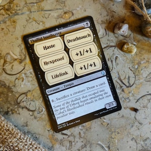 May include: A Magic: The Gathering card, "Thallid Soothsayer," with text boxes for Haste, Hexproof, and Lifelink. The card also features Deathtouch and +1/+1. The card is black with white text and is on a textured surface.