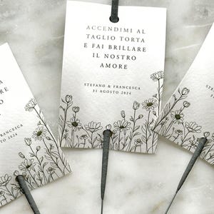 Könnte beinhalten: Weiße Karte mit schwarzem Text und einem floralen Rand. Der Text lautet "Accendimi al taglio torta e fai brillare il nostro amore" und "Stefano & Francesca 31 Agosto 2024".