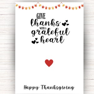 K&ouml;nnte beinhalten: Eine wei&szlig;e Karte mit einer schwarz-wei&szlig;en Grafik, auf der "Give thanks with a grateful heart" und ein rotes Herz steht. Die Karte hat auch eine Girlande aus Herbstbl&auml;ttern und ein rotes Herz unten, auf dem "Happy Thanksgiving" steht.