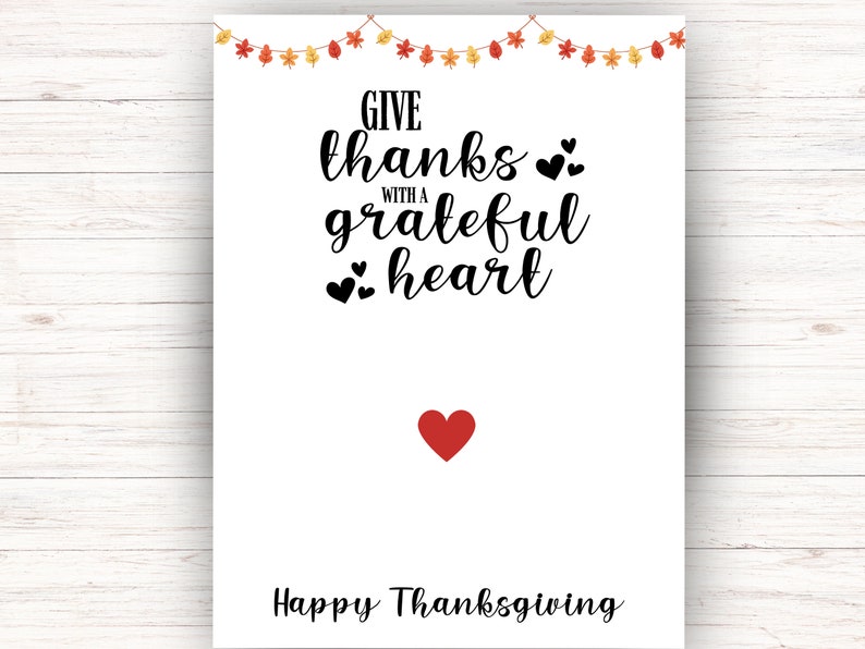 K&ouml;nnte beinhalten: Eine wei&szlig;e Karte mit einer schwarz-wei&szlig;en Grafik, auf der "Give thanks with a grateful heart" und ein rotes Herz steht. Die Karte hat auch eine Girlande aus Herbstbl&auml;ttern und ein rotes Herz unten, auf dem "Happy Thanksgiving" steht.